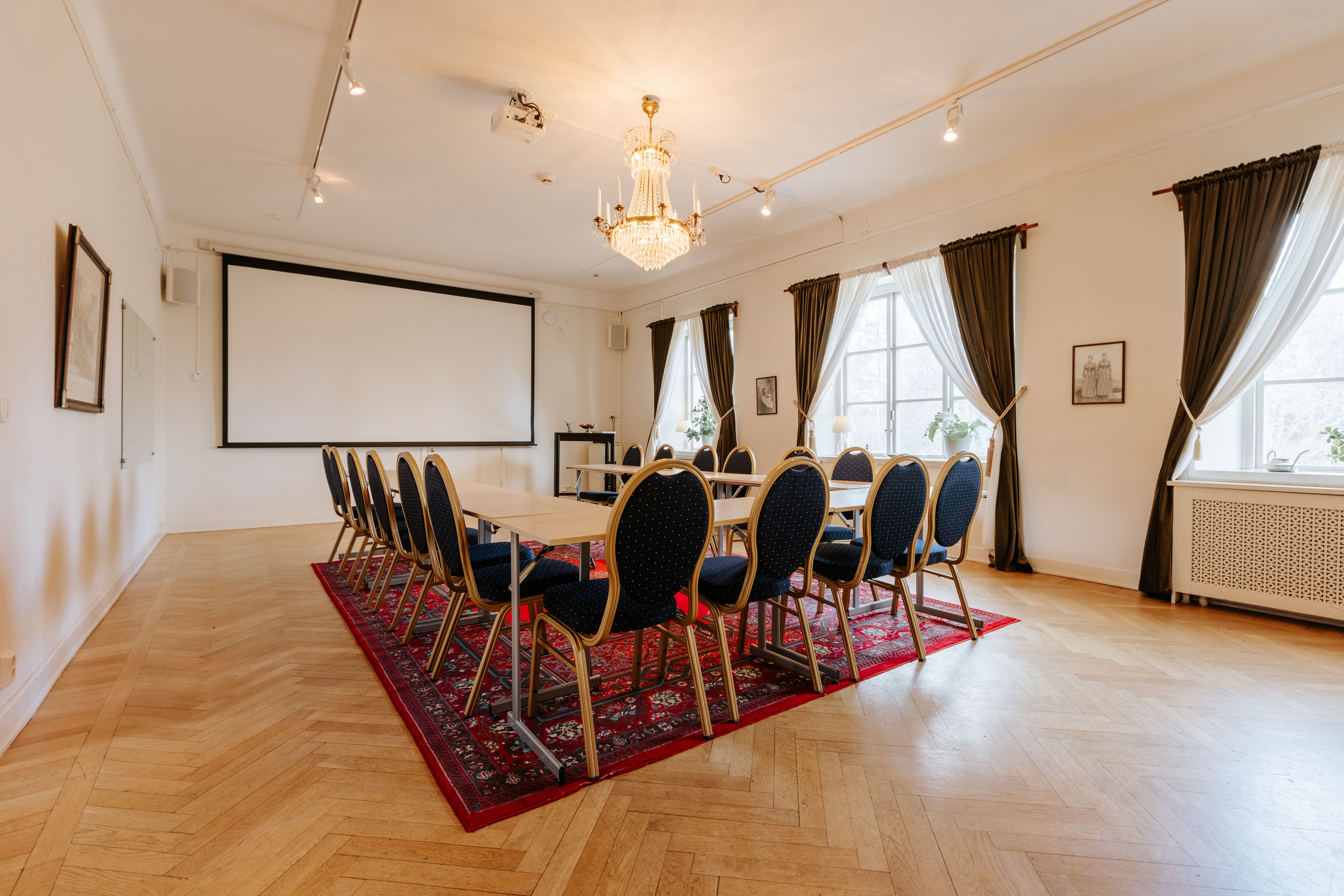 Mötesrum med rund bordssittning, mörka gardiner och stor projektor, beläget i Sala Silvergruva.