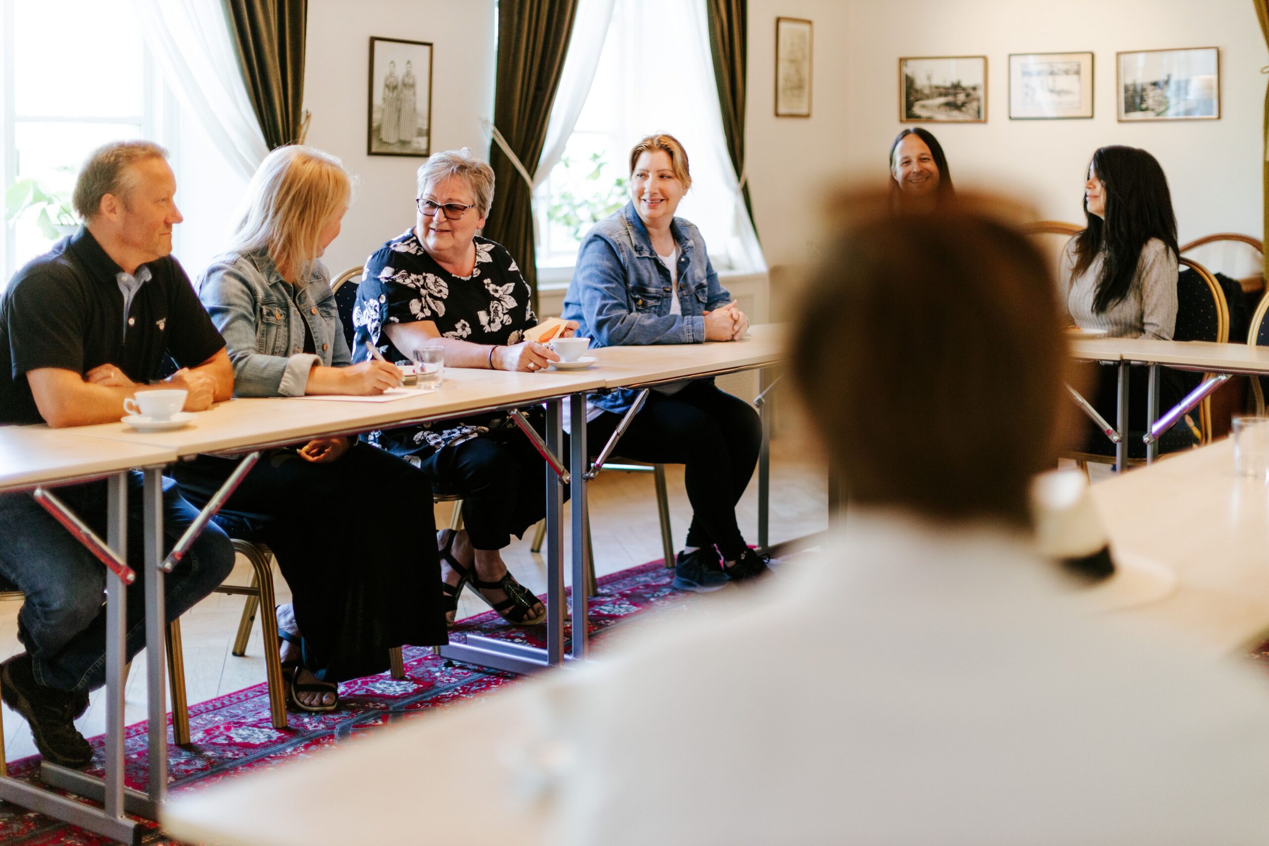 Mötesdeltagare samlade runt ett bord i en ljus konferenslokal, med fokus på samarbete och diskussion.