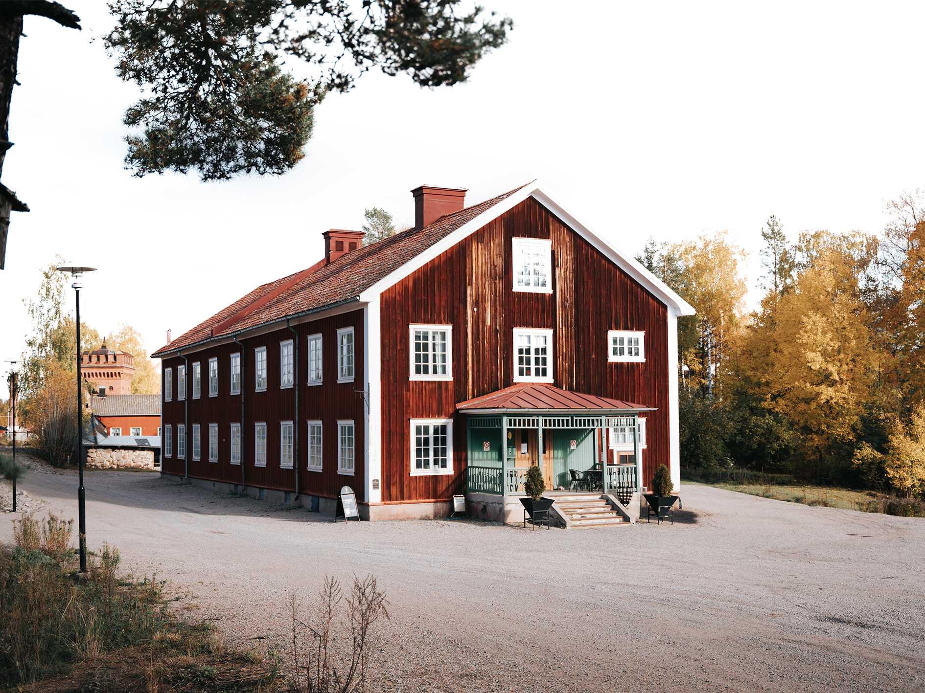 Röd byggnad med vit knutkning och gröna detaljer, omgiven av träd och höstfärger, belägen vid Sala Silvergruva.