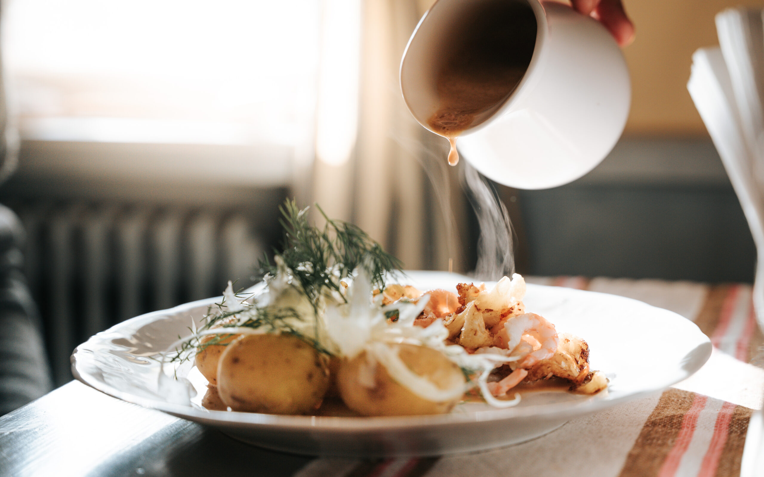 Upphettade potatisar med fisk, lökskivor och en brun sås hälls över, serverat i en hemtrevlig miljö.