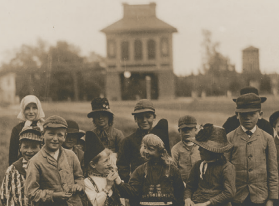 Grupp av barn i historisk klädsel framför Sala Silvergruva, med byggnader i bakgrunden. En nostalgisk fotomiljö.