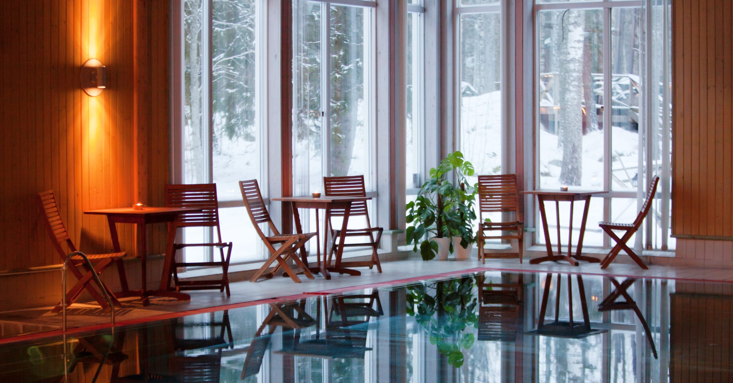 Avkopplande spaområde med pool, träbord och vinterlandskap genom fönstren, skapar en lugn atmosfär.