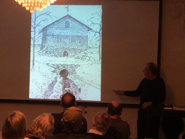 En föreläsare pekar på en historisk teckning av Sala Silvergruva, med åhörare i bakgrunden.